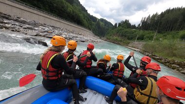 Group engaged in white water rafting on a river surrounded by green mountain scenery, all wearing helmets and life jackets. | © Adventure Service Outdoorsports 