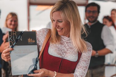 Woman enjoying an event, holding a certificate and wearing traditional attire. | © Zell am See-Kaprun Tourismus