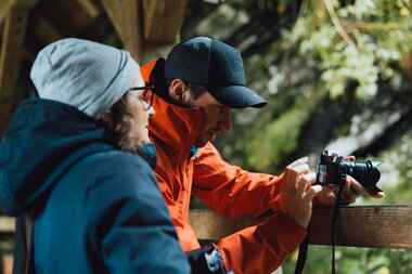 Two people at an outdoor photography workshop, one points at a camera while the other observes attentively. | © Evolumina
