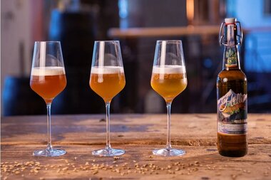 Three glasses with a beverage and a bottle on a wooden surface. | © Grand Hotel Zell am See