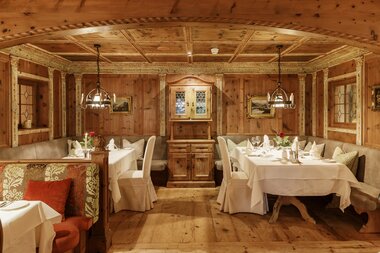 Cozy tables set in a rustic, wood-paneled dining room with windows, wooden ceiling, and chandeliers. | © Salzburgerhof Zell am See
