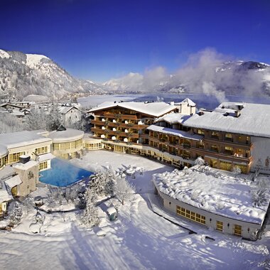A snow-covered resort in the mountains with multiple buildings and a swimming pool, surrounded by winter scenery. | © Salzburgerhof Zell am See