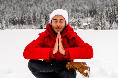 Person meditating in a snowy landscape with mountains in the background, winter scenery | © Katharina Eder Arts 