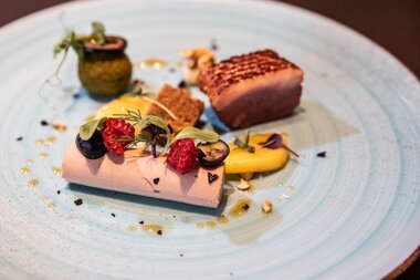 Elegant plated dish featuring fish, fruit, vegetables, and garnishes on a blue plate. | © Tauern SPA