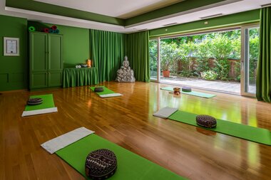 Interior of a yoga retreat with green mats, cushions, and view of garden outside. | © 5*S Hotel Salzburgerhof Zell am See