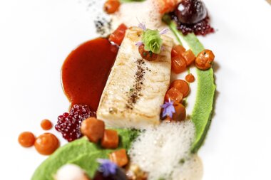 Elegant dish with fish, vegetables, and gourmet sauces, artistically presented. | © 5*S Hotel Salzburgerhof Zell am See
