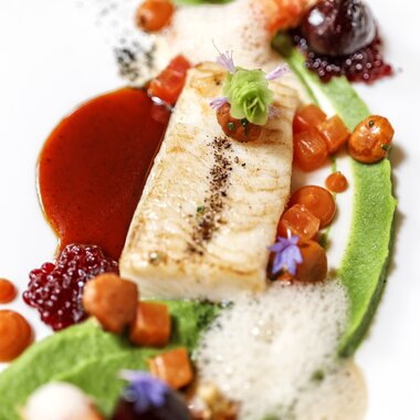 Elegant dish with fish, vegetables, and gourmet sauces, artistically presented. | © 5*S Hotel Salzburgerhof Zell am See
