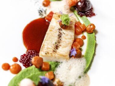 Elegant dish with fish, vegetables, and gourmet sauces, artistically presented. | © 5*S Hotel Salzburgerhof Zell am See