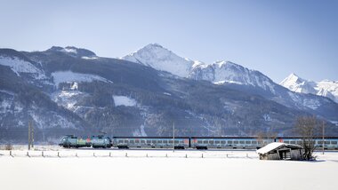 A train travels through a snowy landscape with mountains in the background. | © ÖBB, Harald Eisenberger