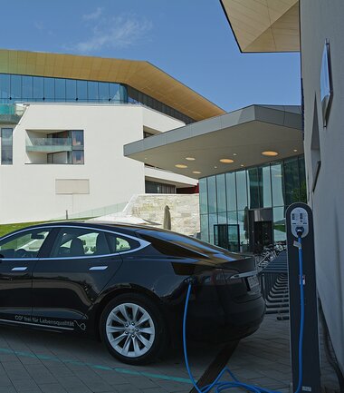 Electric vehicle charging station in front of Tauern Spa with a car being charged, on a sunny day with modern architecture in the background. | © TAUERN SPA Zell am See-Kaprun