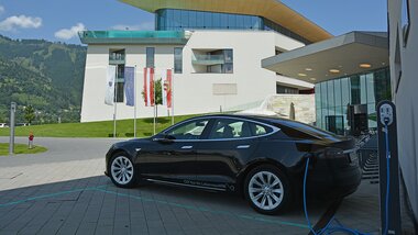 Electric vehicle charging station in front of Tauern Spa with a car being charged, on a sunny day with modern architecture in the background. | © TAUERN SPA Zell am See-Kaprun
