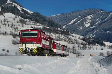 A train of the Pinzgauer Lokalbahn travels through a snowy winter landscape in the mountains. | © Salzburg AG