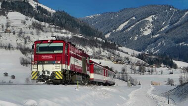 A train of the Pinzgauer Lokalbahn travels through a snowy winter landscape in the mountains. | © Salzburg AG