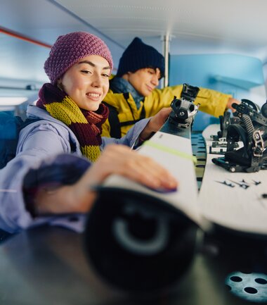 Two people in winter clothing on a train, one writing in a notebook, the other packing skis. | © Westbahn, Ulrich Zinell