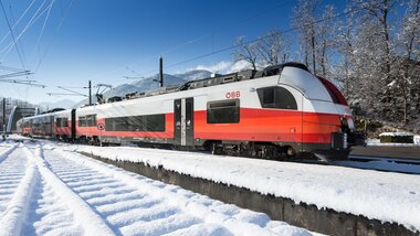 A modern OEBB electric train travels through a snowy landscape with trees in the background. | © Kriechbaum 