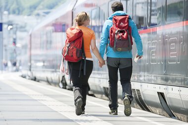 Two people with backpacks walking beside a train at a station. | © Harald Eisenberger