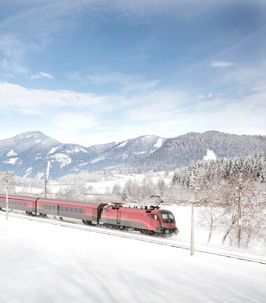 A Railjet train traveling through a snowy winter landscape with mountains in the background. | © ÖBB, Harald Eisenberger