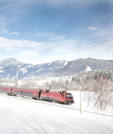 A Railjet train traveling through a snowy winter landscape with mountains in the background. | © ÖBB, Harald Eisenberger