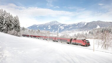 A Railjet train traveling through a snowy winter landscape with mountains in the background. | © ÖBB, Harald Eisenberger