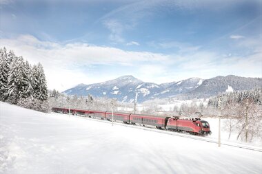A Railjet train traveling through a snowy winter landscape with mountains in the background. | © ÖBB, Harald Eisenberger