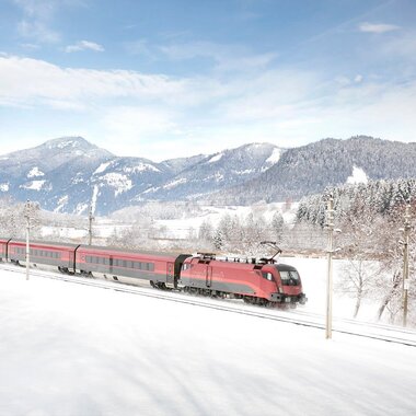 An ÖBB train traverses a snowy winter landscape with mountains in the background. | © ÖBB, Harald Eisenberger