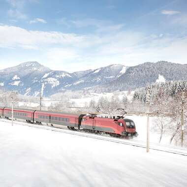 An ÖBB train traverses a snowy winter landscape with mountains in the background. | © ÖBB, Harald Eisenberger
