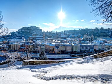 Winter skyline of Salzburg with snow-covered ground, trees, and bright sun | © Tourismus Salzburg GmbH
