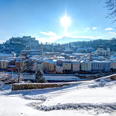 Winter skyline of Salzburg with snow-covered ground, trees, and bright sun | © Tourismus Salzburg GmbH