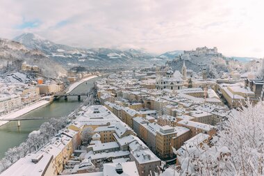 Snow-covered cityscape of Salzburg in winter with river, bridges, and historic buildings | © SalzburgerLand Tourismus