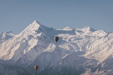 Hot air balloons flying in front of snow-covered mountains in the Alps.