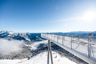 Viewing platform on a suspension bridge over snowy mountain landscape with clouds. | © Schmittenhöhebahn AG, Johannes Radlwimmer