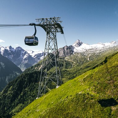 Cable car and cabin in a mountain landscape with mountains in the background and a green hillside. | © Kitzsteinhorn 