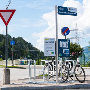 E-bike charging station with bicycles, signs, and traffic light near a bike lane. | © Zell am See-Kaprun Tourismus
