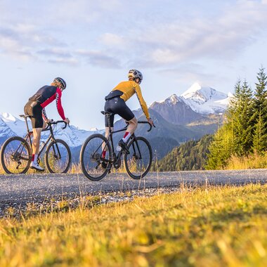 Two cyclists riding in a mountainous landscape with snow-capped peaks in the background during a gravel ride. | © SalzburgLand Tourismus