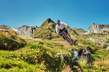 Mountain biker on an uneven trail in mountainous terrain under a clear sky. | © Kitzsteinhorn