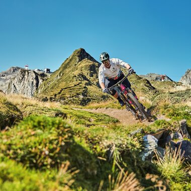 Mountain biker on an uneven trail in mountainous terrain under a clear sky. | © Kitzsteinhorn