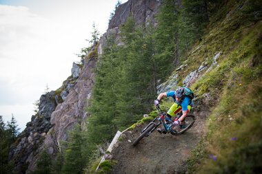 Mountain biker on a steep trail with rocks and pine trees near Kitzsteinhorn in Kaprun. | © David Schultheiß