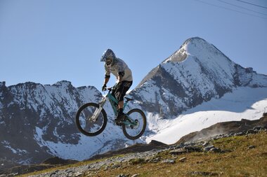 Mountain biker jumping over a mountain landscape with snow-capped peaks in the background.