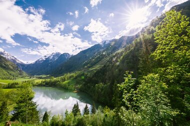 Scenic view of a lake in a valley surrounded by lush green mountains with a sunny sky and reflection on the water. | © Zell am See-Kaprun Tourismus