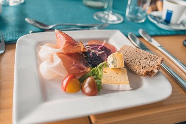 Bread, cheese, cold cuts, tomatoes, and yogurt on a white plate for breakfast. | © Johannes Radlwimmer