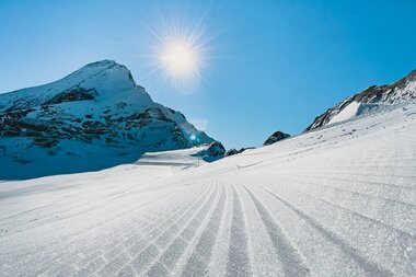 Smooth, groomed ski slope in a snowy mountain landscape under sunlight. | © Johannes Radlwimmer