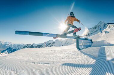 Skier jumping in a snowpark on Kitzsteinhorn with snow-covered mountains in the background. | © Johannes Radlwimmer