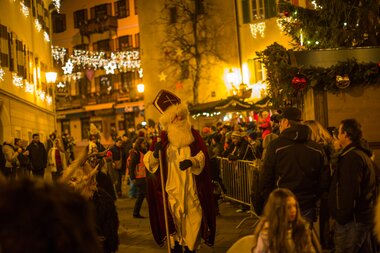 Festive street scene with Santa Claus, Krampuses, and many people under Christmas lights. | © Nikolaus Faistauer Photography
