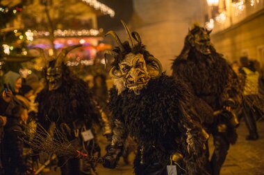 People dressed in Nikolaus and Krampus costumes at a traditional event at night, illuminated by warm lighting. | © Nikolaus Faistauer Photography