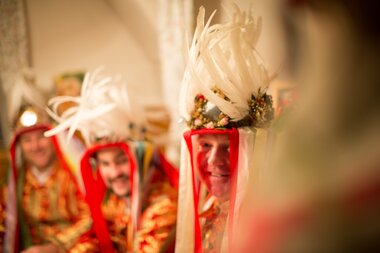 People in traditional costumes with colorful hats and feather decorations at a festive event.