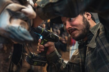A man demonstrates an electric drill in a crowded, lively setting, working on a surface. | © Zell am See-Kaprun Tourismus