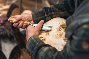 Hands of a woodcarver shaping a wooden figure with a carving knife. | © Zell am See-Kaprun Tourismus