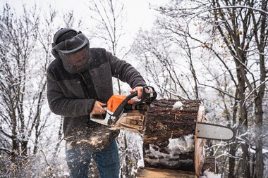Person cutting wood with a chainsaw in a forest during winter, surrounded by trees. | © Zell am See-Kaprun Tourismus