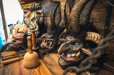 Various carved masks and figures, including a buffalo head and mythological creature, displayed on a wooden shelf. | © Zell am See-Kaprun Tourismus