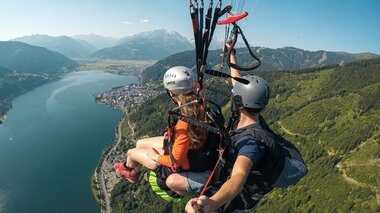 Two people paragliding over a lake with mountains in the background, overlooking the landscape and water. | © FalkenAir Tandemparagliding